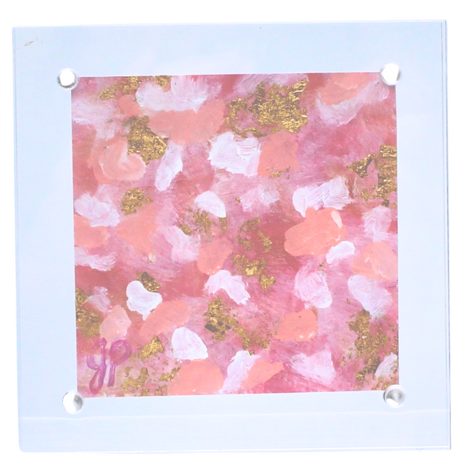 Small abstract painting in a clear acrylic block measuring 4 x 4 inches, The abstract looks like pink white and gold confetti. 