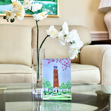 Load image into Gallery viewer, Denny Chimes Acrylic Block Art. This Alabama Crimson Tide free standing acrylic block art is vertical and features the famous Bell Tower landmark that is in The Quad at The University of Alabama. This is a print on an acrylic block of a bell tower with  flowering trees and plants. Roll Tide!