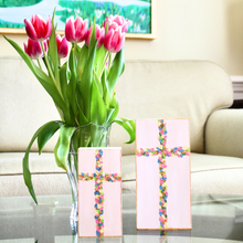 Load image into Gallery viewer, Flowered Crosses are original works of art on wood panels. These two crosses are vertical artworks in two different sizes. They have shades of pink, yellow, blue, coral, gold and green on a white backrground. The edge is outlined in gold. They sit on a table with a vase of flowers beside them and a sofa behind them.
