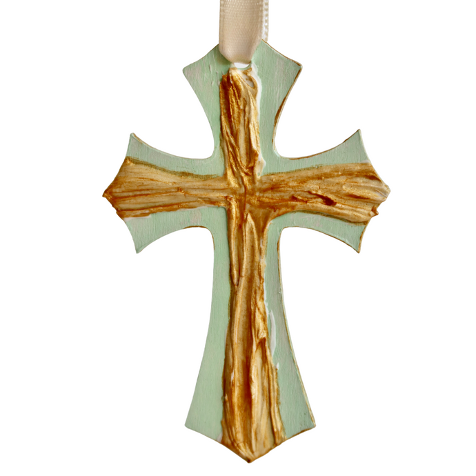 The Green Cross Ornament is an original work of art. This small cross is gold and has a raised texture. It is on a green background that is also the shape of a cross and has a cream riboon.