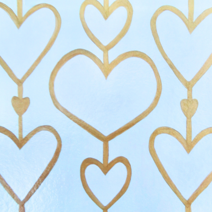 Heartstrings XII Liner for the 12 x 12 inch Acrylic Tray.  This liner insert has 3 rows of hearts. They are attached by a gold line and each heart is outlined in gold. This is a white on cream pattern. With 2 smaller gold hearts in bwtween.This liner can also be used as a placemat.