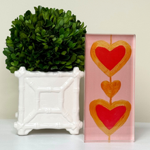 Load image into Gallery viewer, Heartstrings XIII acrylic block art featuring pink and gold heart design by Jeanne Player, displayed on a shelf. This is a shelf sitter made of an acrylic block. Cute, colorful and stylish pop art. Pink, red and gold colors. a perfect gift for loved ones.