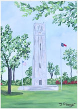 Load image into Gallery viewer, NC State Bell Tower Art on a Free Standing Acrylic Block styled on a coffee table beside a vase of orchids. This is a vertical landscape artwork of NCSU Memorial Belltower reproduced on an acrylic block. The belltower is in grassy field with blooming trees and shubbery. It is a small 5 x 7 inch block perfect to give for NC State graduation gift or alumni gift. 
