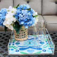 Load image into Gallery viewer, A square acrylic tray with handles. The design on the bottom of the tray is modern and abstract with shades of blue and green on a white background. This tray is holding a vase of hydrangeas and 2 champagne glasses.