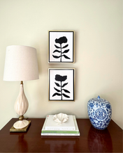 Load image into Gallery viewer, Decorative items on a wooden surface with framed black floral art and a lamp.
