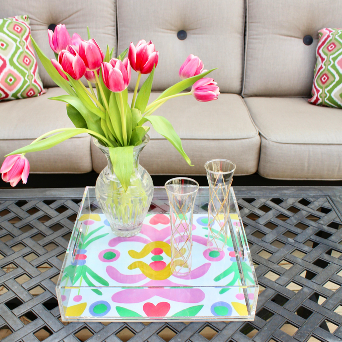 Square Acrylic Tray with a colorful bottom liner. It is a modern and abstract design with shades of pink, yellow, red, green, and purple on a white background. On the tray you see two champagne glasses and a vase of tulips.
