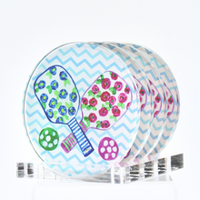 Load image into Gallery viewer, Preppy Pickleball Coaster Set. This set of round coasters have 2 pickleball paddles with a blue and pink floral design, green leaves, striped handles and a green and pink ball. They are on a blue and white chevron background. You can choose the option of a clear acrylic stand.