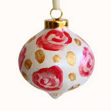 Load image into Gallery viewer, This is an abstract floral art design ornament. It has flowers in shades of pink and red with gold dots in between them on a white background. It has a gold top and a white ribbon.