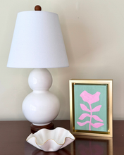Load image into Gallery viewer, White lamp with a white shade, pink floral artwork in a gold frame, and a white ceramic bowl on a wooden surface.