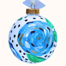 Load image into Gallery viewer, A fun and whimsical blue floral ornament. This round abstract floral has shades of blue, white ,black and gold with green leaves. This original hand painted ornament is round an has a black dot s on a white background. Original abstract floral Christmas ornament with blue, white, gold, and green botanical details, ideal for collectors and holiday gift giving.