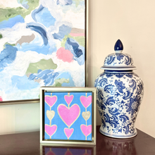 Load image into Gallery viewer, Original pink heart painting on blue canvas in a gold float frame by Jeanne Player Fine Art.
Contemporary square heart artwork featuring multiple pink hearts with gold details on a blue background.