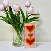Load image into Gallery viewer, Freestanding acrylic heart artwork featuring Jeanne Playerās original painting reproduced with vibrant pink and gold colors, ideal for desks, bookshelves, bedrooms, and offices.