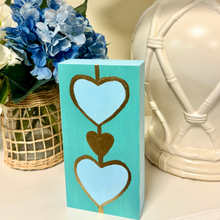 Load image into Gallery viewer, Contemporary abstract heart artwork with sky blue hearts and metallic bronze gold details on turquoise background.
Coastal heart painting on wood panel designed for beach house decor and colorful modern interiors.