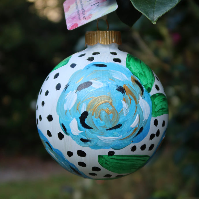 A fun and whimsical blue floral ornament. This round abstract floral has shades of blue, white ,black and gold with green leaves. This original hand painted ornament is round an has a black dot s on a white background.