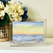 Load image into Gallery viewer, An abstract beach landscape painting on paper. Framed in an acrylic frame. The art has shades of blue, gray, white, yellow, and orange. It is initialed by the artist JP on the front.
