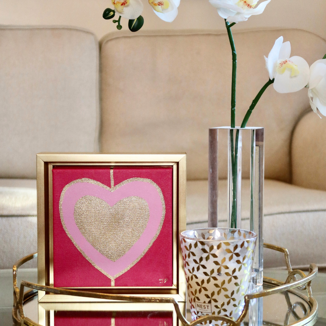 Heart Art Acrylic on Canvas. Gold and pink hearts on red background. This square heart pop art painting comes in a gold frame and is dislplayed by a vase of orichids with a sofa in the background. Trending Maximalist art.