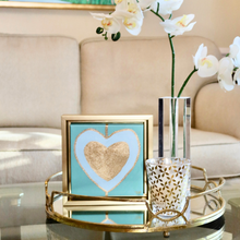 Load image into Gallery viewer, Heart Art on Canvas. Gold and blue hearts on a green background in a square gold frame. This is a modern style heart paintng. Colorful and happy hearts styled on a coffee table beside a vase of orchids  with a white sofa in the backround.
