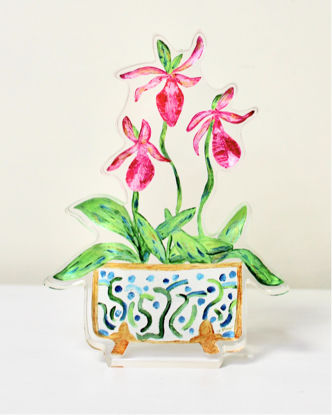 The Ladyslipper Freestanding Acrylic Block is a colorful artwork in acrylic. This cutout acrylic block art has three pink orchid blooms, green leaves in a beautiful cachepot with a fun design in blue and green on a white background with gold feet and outlined in gold.