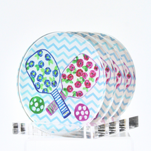 Load image into Gallery viewer, Preppy Pickleball Coaster Set. This set of round coasters have 2 pickleball paddles with a blue and pink floral design, green leaves, striped handles and a green and pink ball. They are on a blue and white chevron background. They come with a clear acrylic stand.
