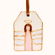 Load image into Gallery viewer, The Pink angel ornament is an original hand painted angel on a ceramic ornament. The background is cream. The angel has a pink dress, white wings, brown hair and a gold halo. The angel is outlined in gold  and the ornament is outlined in gold. It has a gold ribbon for hanging.
