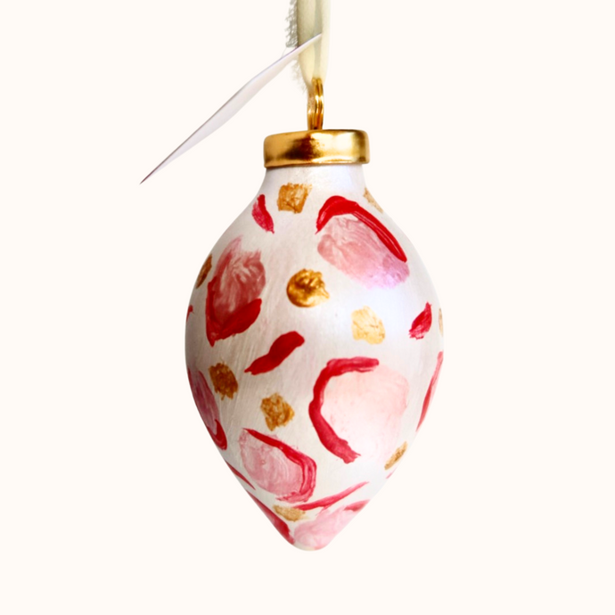 This is an animal print ornament with a gold top. It has shades of pink and red with gold dots. It has a cream raw silk  ribbon for hanging.