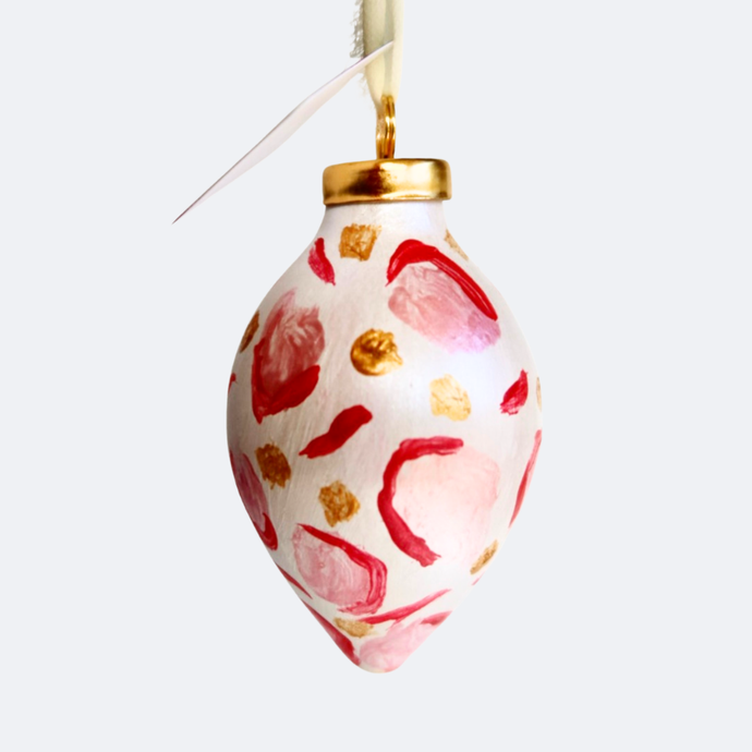 a hand painted christmas tree ornament with an elongated shape. This ornament has a pink, red animal print design with gold dots. it comes with a cream raw silk ribbon for hanging.