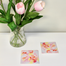 Load image into Gallery viewer, This is an abstract art design on a coaster set. It is shown with a vase of pink tulips. It has shades of pink, orange, yellow and peach on a white background.
