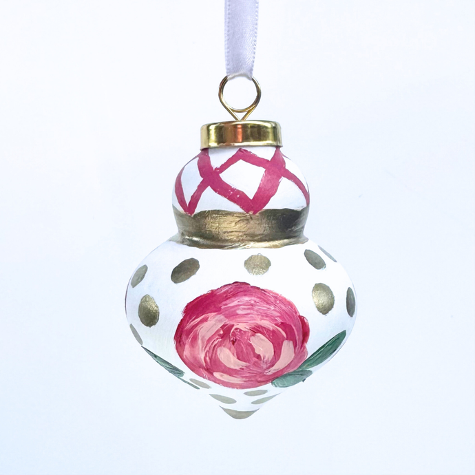 Hand-painted Christmas ornament with abstract pink and red flowers, green leaves, gold dots, and lattice detail. Finial-style round ornament with satin ribbon for hanging, whimsical and unique holiday décor.