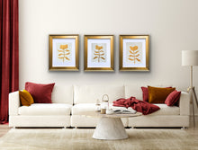 Load image into Gallery viewer, a set of three gold botanicals styled over a white sofa with red pillows and curtains.
