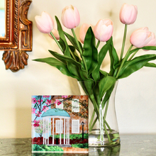 Load image into Gallery viewer, UNC Free Standing Acrylic Block Art is an original painting repoduced on heavy weiight paper and affixed to a free standing acrylic block.  The image is visible from all 4 sides. This mini artwork is displayed on a table with a vase of pink tulips. Artwork of The University North Carolina Chapel Hill Old Well.
