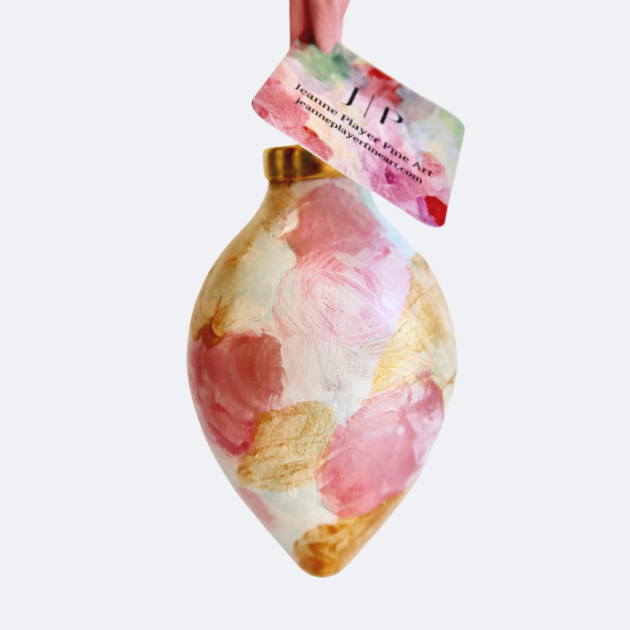 a hand painted original ornament on ceramic. this abstract ornament has shades of pink, white and gold. It has an enlongated shape and a pink silk ribbon