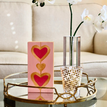 Load image into Gallery viewer, Heartstrings XIII acrylic block artwork featuring vibrant pink, rose, and gold hearts on a clear freestanding acrylic display, creating modern pop art decor for any room.
