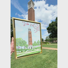 Load and play video in Gallery viewer, Original acrylic painting of Denny Chimes at the University of Alabama featuring the iconic brick bell tower, blooming pink dogwood branches, and lush campus greenery in a gold float frame.

