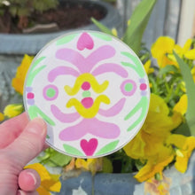 Load and play video in Gallery viewer, A video of a  colorful lucite coaster with an abstract art design. This video shows the front and back of the coaster and has yellow flowers in the background.
