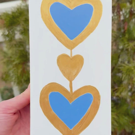 Original royal blue heart painting on wood panel with metallic gold outline and white background by Jeanne Player.
Contemporary abstract heart artwork featuring royal blue hearts and gold detailing on a crisp white background.